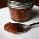 Apple butter on a spoon with a jar of apple butter