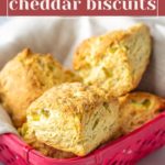 A pink basket lined with cloth holds several golden brown Hatch Cheddar Biscuits, each bursting with savory flavor.