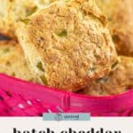 Close-up of golden brown Hatch Cheddar Biscuits with visible green pepper pieces in a pink basket, labeled "hatch cheddar biscuits.