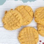 Five classic peanut butter cookies with a crisscross pattern on top are arranged on a white wooden surface. Text above reads "Peanut Butter Cookies." These homemade treats showcase the timeless charm of peanut butter cookies.