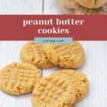 Four freshly baked peanut butter cookies rest on a white wooden surface, with more peanut butter cookies stacked in a jar behind them. Text overlay reads "peanut butter cookies.