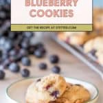 Two blueberry cookies on a small plate with fresh blueberries and more blueberry cookies cooling on a baking rack in the background. Text overlay reads "Blueberry Cookies. Get the recipe at stetted.com.