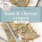Two plates with gluten free crepes filled with ham and cheese, garnished with fresh herbs. A fork and knife rest on one plate. Text overlay highlights the dish and its simple gluten-free recipe.