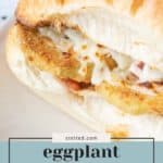 A close-up of an eggplant parmesan sandwich featuring crispy breaded eggplant, gooey melted cheese, and savory sauce on a fresh white bun.