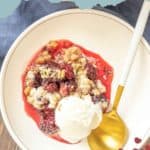 A plate of blackberry crisp topped with vanilla ice cream, served with a gold spoon on a white plate, creates the perfect dessert moment.