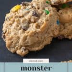 Close-up of three chunky monster cookies packed with oats, chocolate chips, and colorful candy pieces. Text label reads "monster cookies – fully loaded snack.
