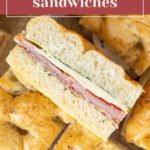 A close-up of pressed Italian sandwiches filled with sliced meats and cheese, layered inside golden focaccia bread. These irresistible pressed Italian sandwiches are perfect for satisfying any craving.