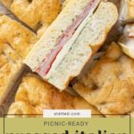 Sliced Pressed Italian Sandwiches with layers of meat, cheese, and vegetables on focaccia bread, arranged on a wooden surface. Text overlay reads "Picnic-ready Pressed Italian Sandwiches.