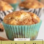 A close-up of a Snickerdoodle Muffin in a blue paper liner, with more Snickerdoodle Muffins in the background and a label reading "snickerdoodle muffins.
