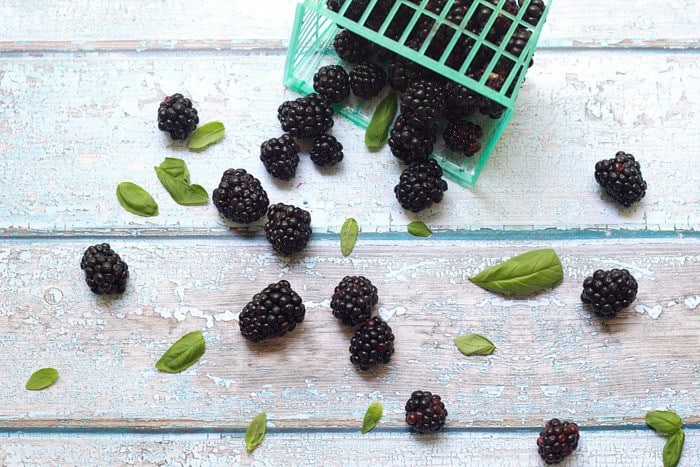 Blackberries and basil scattered on a weathered blue table.