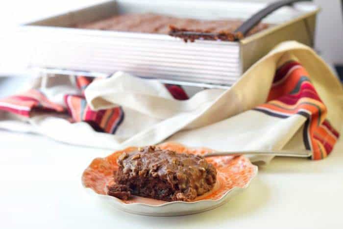 A slice of Texas sheet cake on a dessert plate with the pan of cake behind.