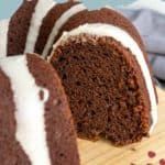 A sliced chocolate pumpkin bundt cake with white icing is displayed on a wooden board, highlighting the rich swirls of this festive chocolate pumpkin bundt dessert.