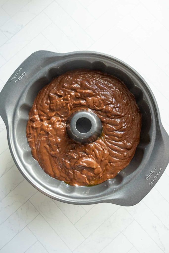 A bundt cake pan filled with rich chocolate pumpkin bundt batter sits on a white tile surface.