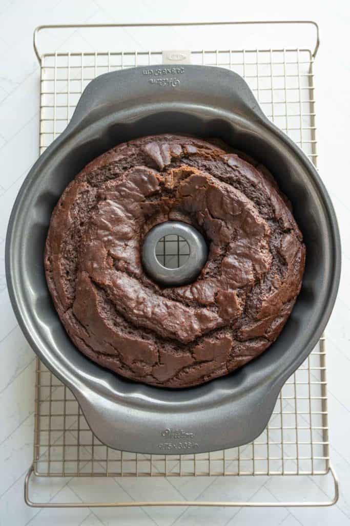 A chocolate pumpkin bundt cake in a nonstick bundt pan rests on a wire cooling rack.