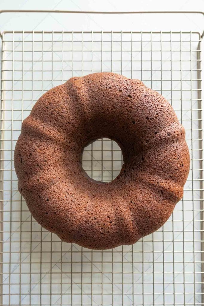 A chocolate pumpkin bundt cake rests on a metal cooling rack placed on a light-colored surface.