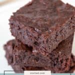 Three thick, fudgy brownies are stacked on a white surface. Text overlay at the bottom reads “fudgy brownies.”.