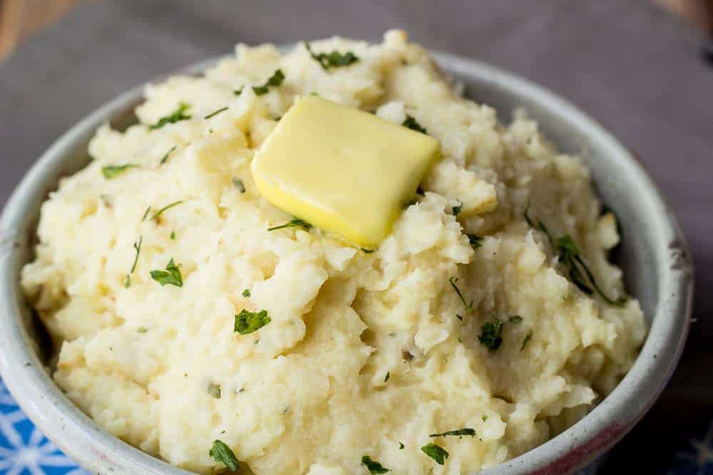 A bowl of mashed celery root with herbs and butter on top.