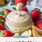 A hand dips a strawberry into a jar of creamy Peanut Butter Fruit Dip, surrounded by fresh strawberries and crisp apple slices.