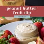 A jar of creamy Peanut Butter Fruit Dip is surrounded by fresh strawberries and apple slices on a white plate, with a bag of peanut powder in the background.