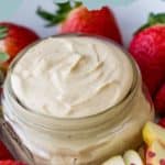 A glass jar of luscious Peanut Butter Fruit Dip surrounded by fresh strawberries and apple slices, with text reading "Peanut Butter Fruit Dip.