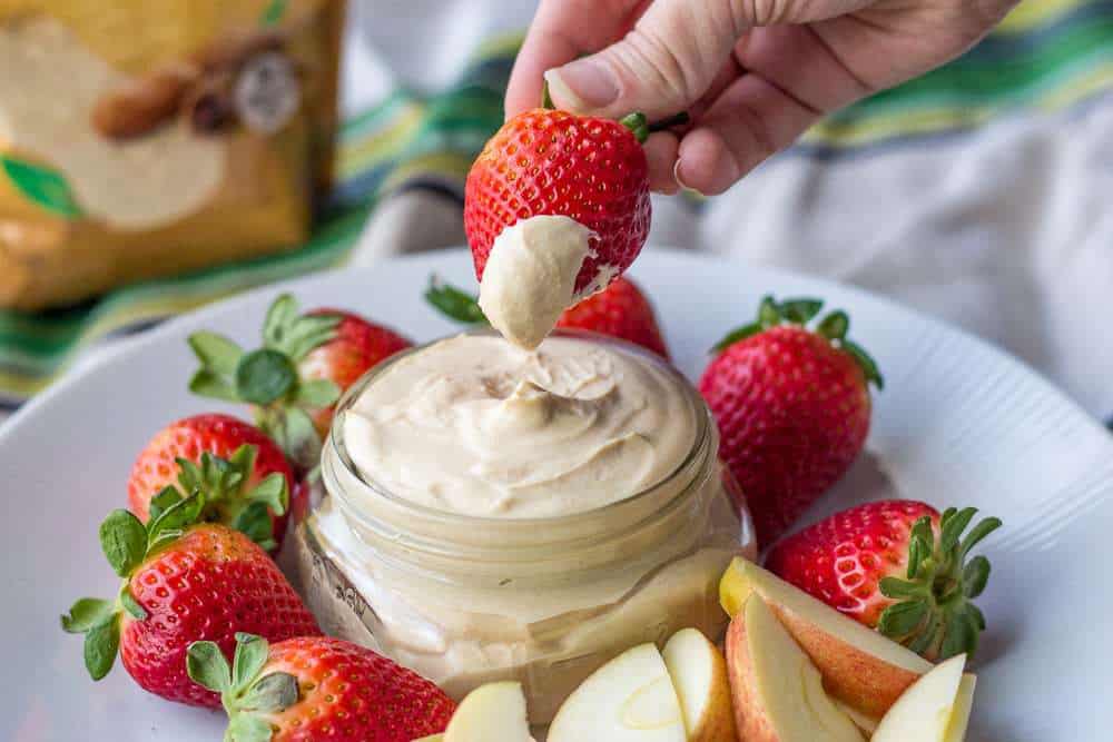 A person dipping a strawberry into peanut butter fruit dip.