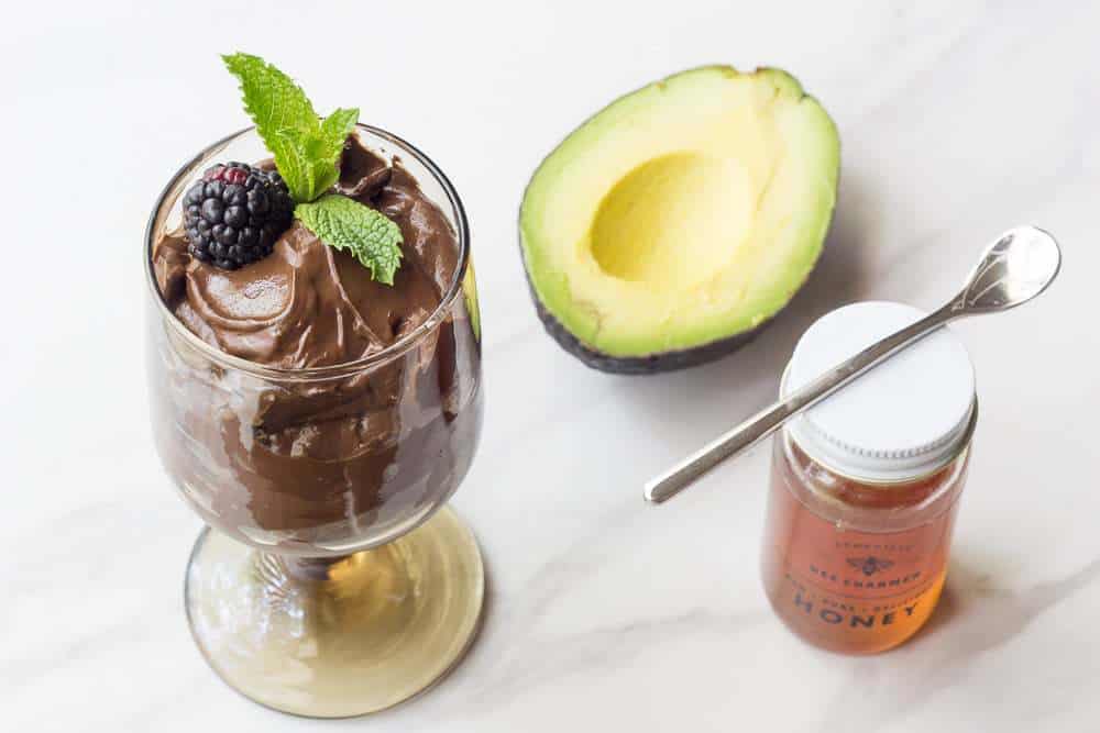 Chocolate avocado mousse in a dessert cup next to a half avocado and jar of honey.
