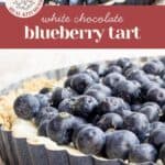 A blueberry white chocolate tart with a crumb crust and creamy white chocolate filling, topped with fresh blueberries, displayed in a fluted tart pan.