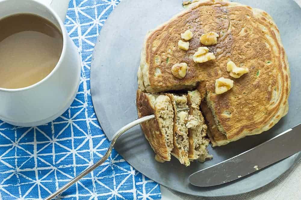 A plate of zucchini bread pancakes with a fork cutting a wedge out.