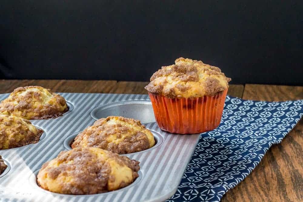 A maple walnut muffin sitting on top of a muffin pan with more muffins in it.