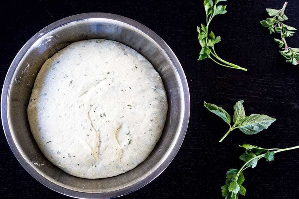 A bowl of pizza dough with herbs.