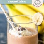 A glass of chunky monkey smoothie—chocolate peanut butter banana goodness—topped with whipped cream, chocolate chips, a paper straw, and a banana slice, with bananas in the background.