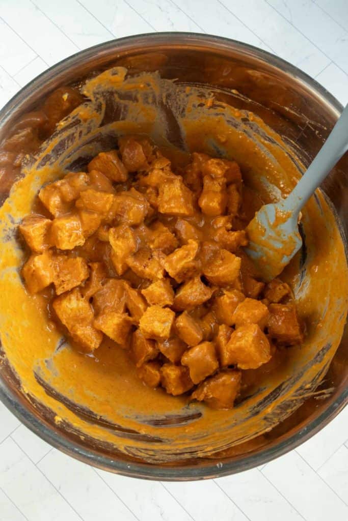 Cubed bread pieces are coated in a pumpkin bread pudding batter mixture inside a large mixing bowl, with a spatula resting on the side.