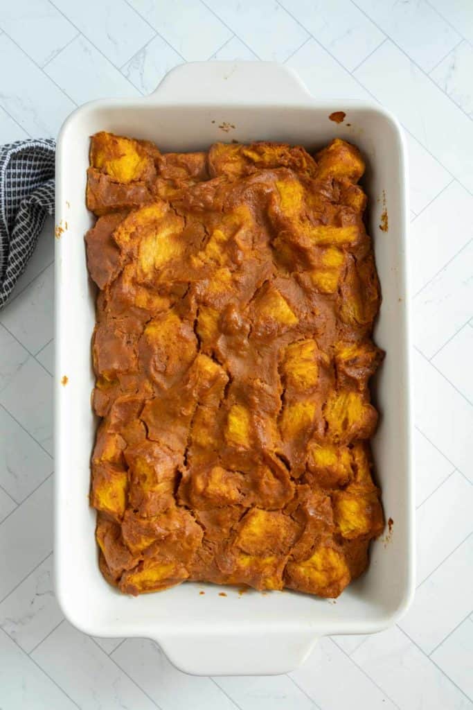 A white rectangular baking dish filled with pumpkin bread pudding, featuring a golden brown top and visible bread pieces.