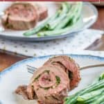 Simple steak roulade filled with fresh herbs, served alongside green beans on a white plate; another plate featuring this flavorful meal appears in the background.
