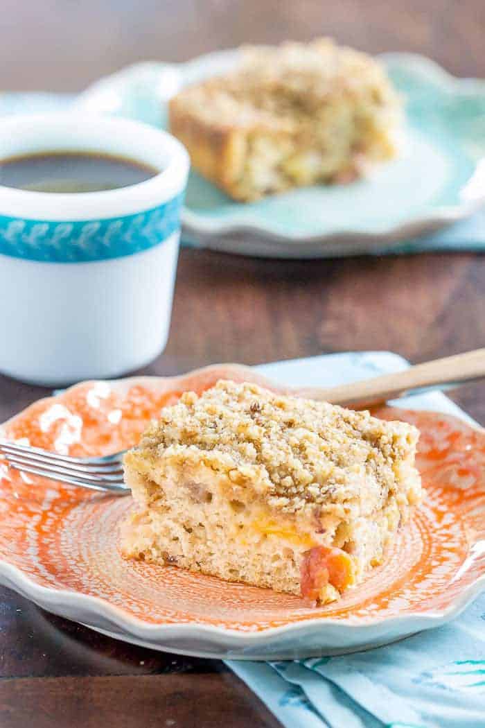 Slice of peach coffee cake with a fork and cup of coffee behind.