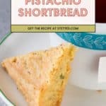 A triangular piece of pistachio shortbread sits on a white plate next to a cup of tea, inviting you to try the delicious pistachio shortbread recipe featured at stetted.com.