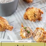 Shrimp hush puppies are displayed on newspaper with a metal cup of dry mix in the background; one shrimp hush puppy is broken open to reveal its savory interior.