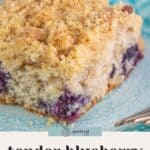A slice of blueberry coffee cake with crumb topping sits on a blue patterned plate next to a fork, showcasing the delicious flavors of classic blueberry coffee cake.