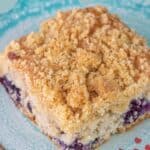 A square slice of blueberry coffee cake with crumb topping sits on a blue plate, text reading "Blueberry Coffee Cake" and "stetted.com" above and below the image, perfectly showcasing this irresistible blueberry coffee cake treat.
