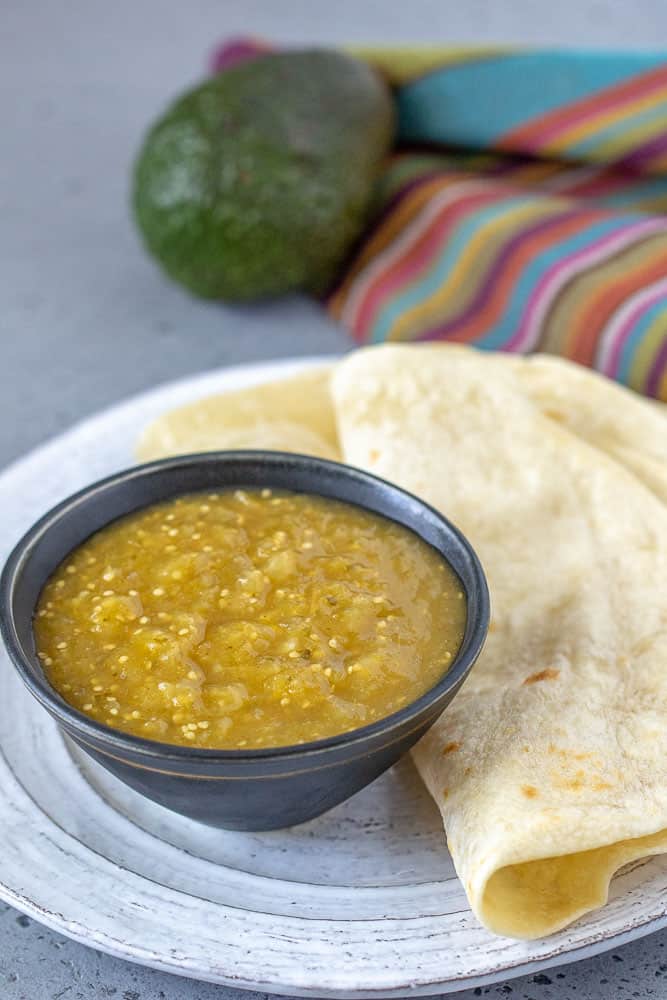 Bowl of tomatillo salsa on plate with . tortillas