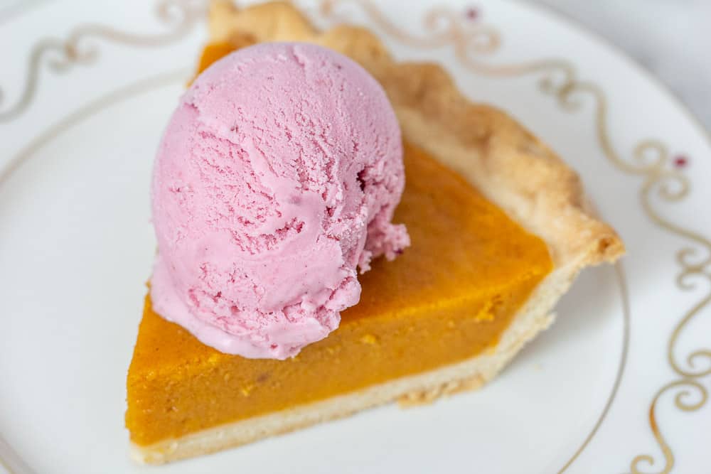 Slice of pumpkin pie with cranberry ice cream on top