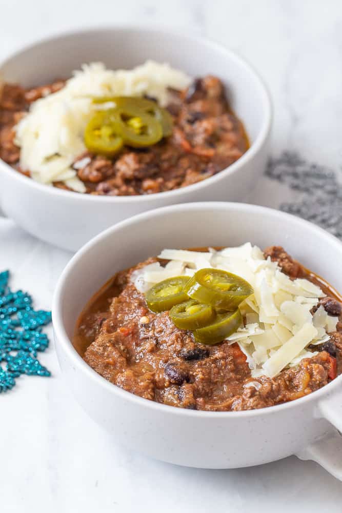 Beef chili in two mugs with cheese and jalapenos 
