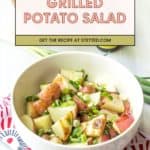 A bowl of grilled potato salad with chopped green onions sits on a patterned cloth; a website banner for the grilled potato salad recipe appears above.