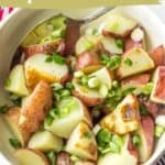 A bowl of grilled potato salad topped with chopped green onions and served with zesty lemon dressing, featuring a spoon for easy serving.
