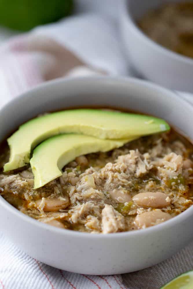 close up of white bean chicken chili in a bowl with avocado