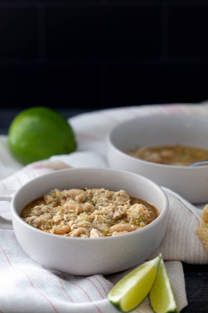 white bean chicken chili in a bowl with a black background and limes