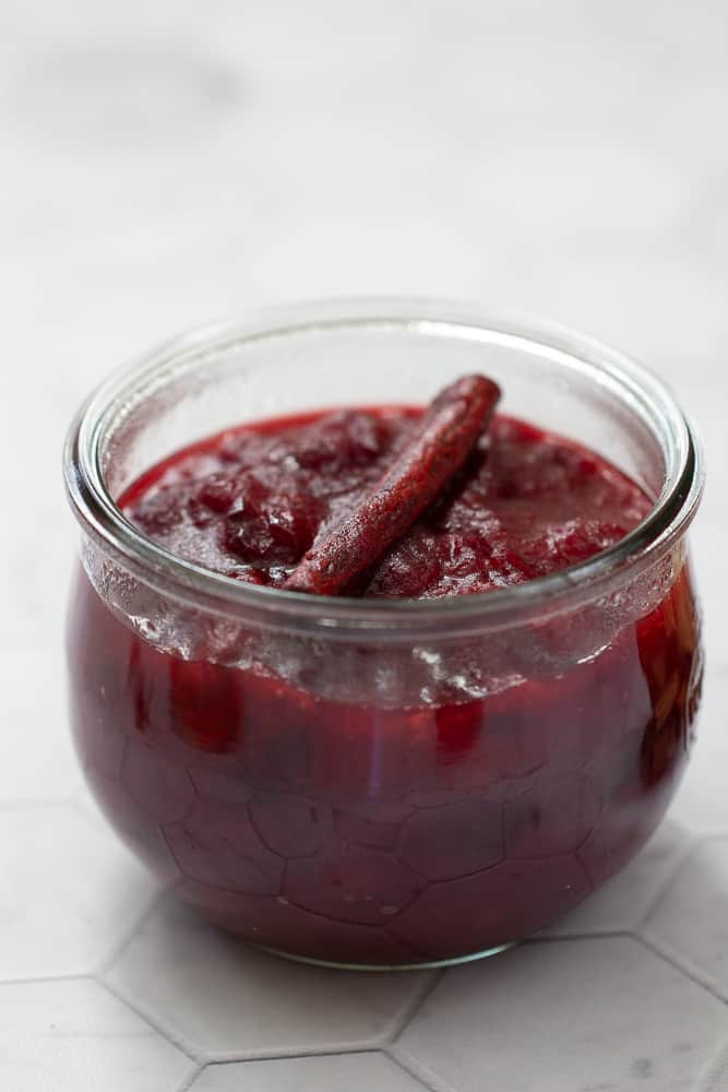 close up of cranberry sauce in glass jar with a cinnamon stick on top