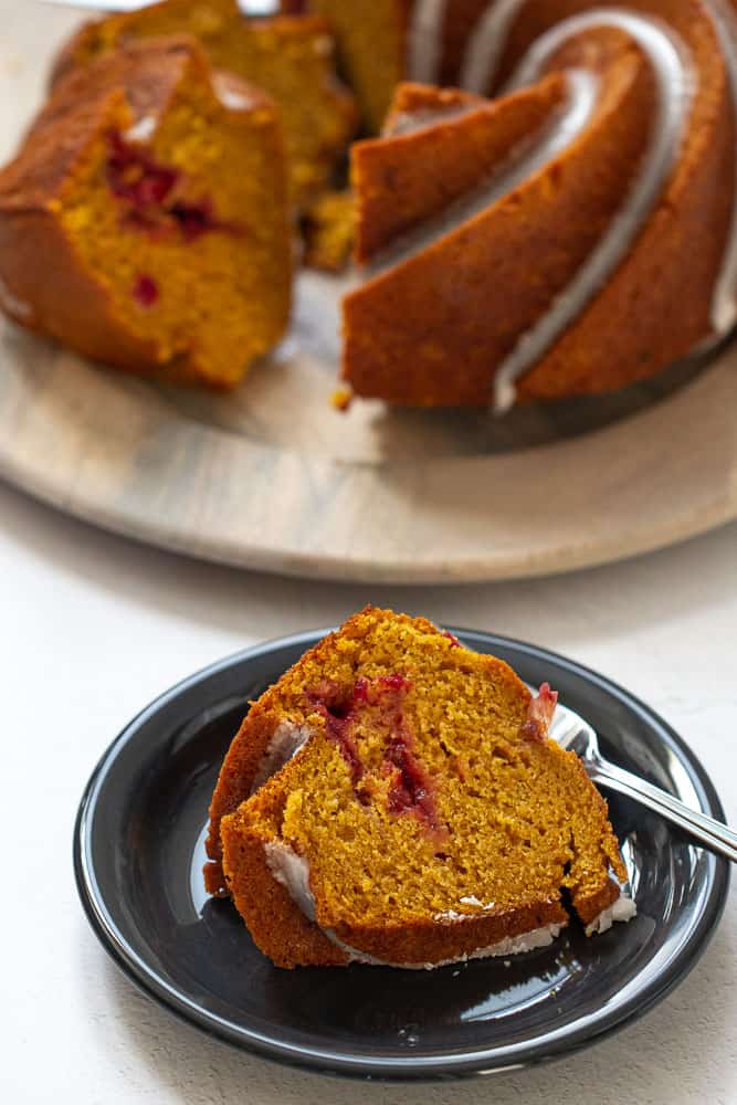 Slice of pumpkin bundt cake with cranberry swirl on a black plate