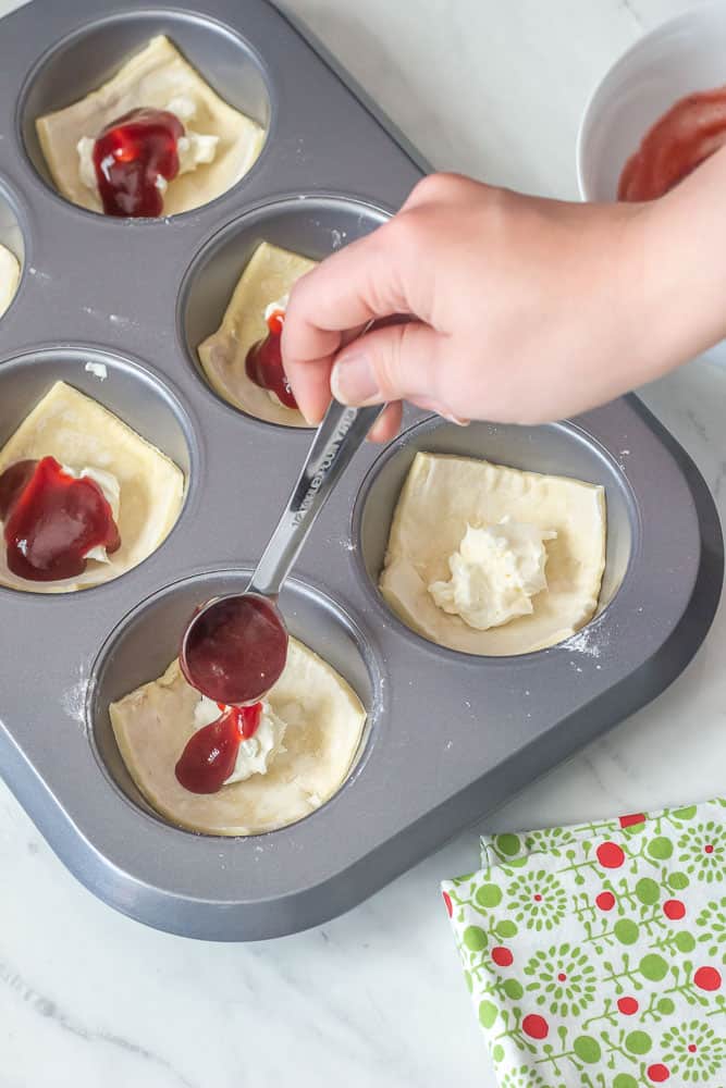 overhead image of hand pouring jam onto cheese danishes in baking pan