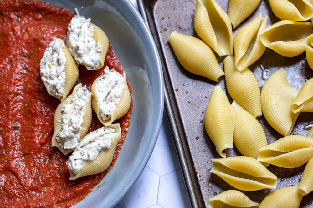 Unstuffed shells on a pan next to stuffed shells in a baking dish.